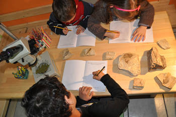 Three young children are sitting at a table and on a block they try to draw the stones in front of them